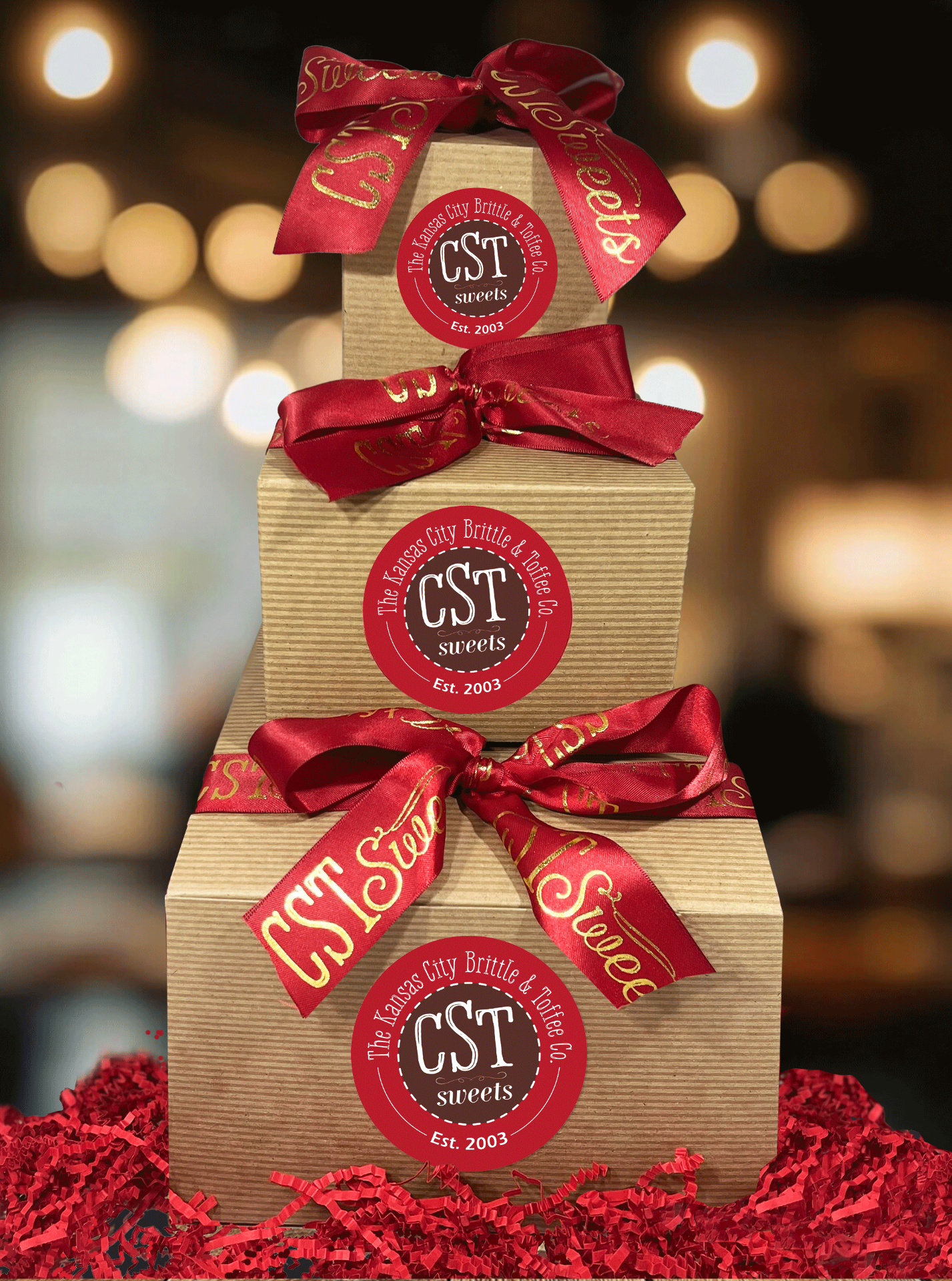 Beutifully boxed, labeled gift boxes in a stack from large to small. Red Ribbons tied in a bow with gold printing with "CST Sweets".